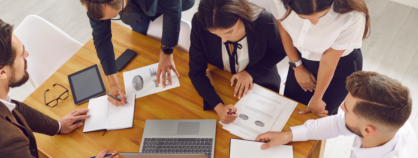 Business People Gathering around Office Desk with Laptop and Working on Project Together